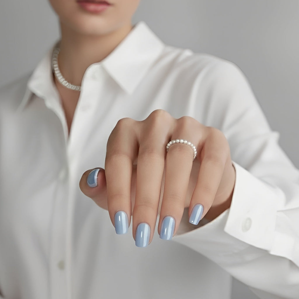 Hand with light blue nail polish wearing a white shirt and pearl necklace.
