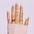 Hand with gold rings and glittery nails against a light purple background