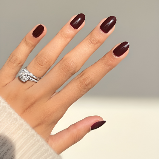 Hand with dark burgundy nail polish wearing a ring on a neutral background